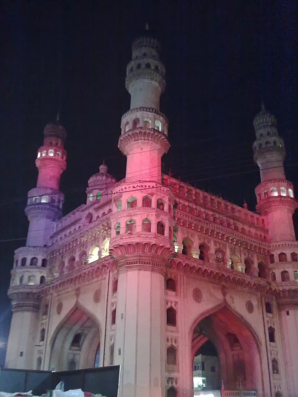 The Charminar in Hyderabad at night, lit in pink and purple against a black sky